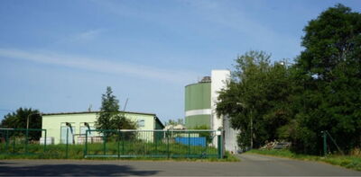 Industriegelände mit grünem Silo, Lagerhalle und eingezäuntem Betriebsgelände