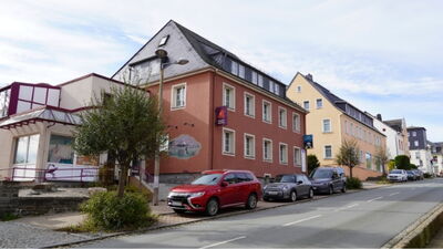 Mehrgeschossiges Wohn- und Geschäftshaus mit rotbrauner Fassade, Schieferdach und Wandmalerei an der Seitenwand