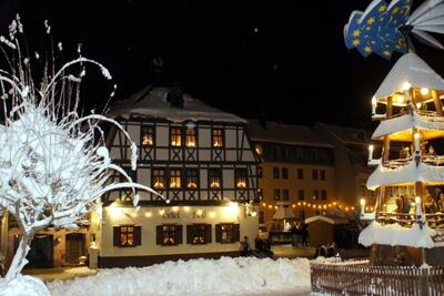 Winterliche Nachtaufnahme eines Fachwerkhotels mit Weihnachtspyramide und verschneitem Marktplatz