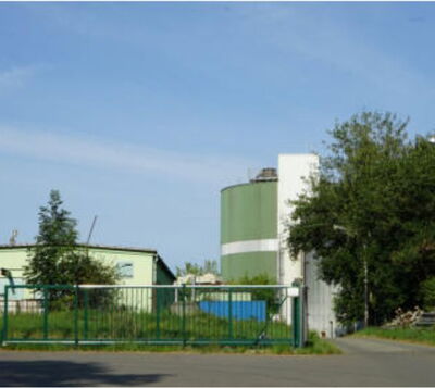 Industriegelände mit grünem Silo, Lagerhalle und eingezäuntem Betriebsgelände