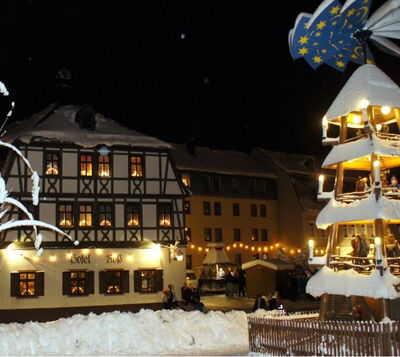 Winterliche Nachtaufnahme eines Fachwerkhotels mit Weihnachtspyramide und verschneitem Marktplatz