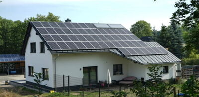 Weißes Einfamilienhaus mit großflächiger Photovoltaikanlage auf dem Satteldach